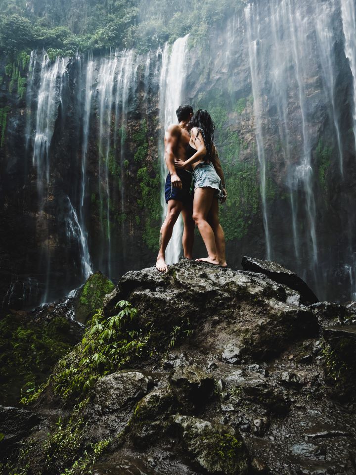 ruta por indonesia cascada de fondo y dos chicos mirando hacia ella cogidos